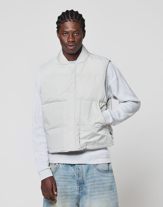 A man with braided hair wears the LIVE FAST DIE YOUNG Basic Cropped Vest in light gray over a gray sweatshirt and faded blue jeans, standing against a plain white background.