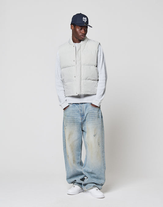Someone wearing a LIVE FAST DIE YOUNG Basic Cropped Vest in light gray over a gray long-sleeve shirt, navy baseball cap, baggy light blue regular-fit jeans, and white sneakers stands against a plain white background.