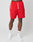 A person models LIVE FAST DIE YOUNG Beach Shorts—bright red with an elastic waistband and white drawstrings—paired with white crew socks and sneakers, against a light gray backdrop. Only the lower half of the body is visible.