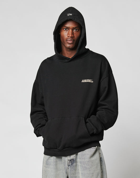A person wears the LFDY Savior Hooded by LIVE FAST DIE YOUNG in black, featuring an oversize fit and a small white chest logo, paired with light blue jeans. The 100% Baumwolle hoodie is shown against a plain light gray background.