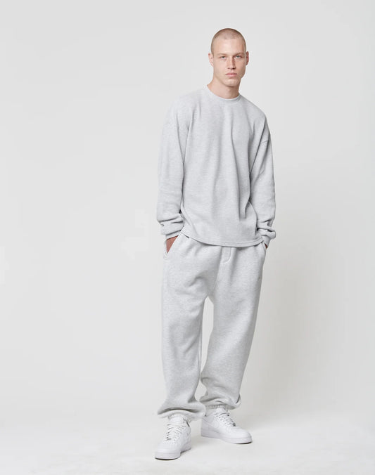 A person with a buzz cut stands against a plain white background, wearing the LIVE FAST DIE YOUNG Blank Waffle Longsleeve in an oversize fit and light gray color, hands in pockets with matching sweatpants and white sneakers.