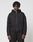 A person with medium-length twisted hair wears the LIVE FAST DIE YOUNG LFDY Active Fleece Hooded Zip in black, styled oversized with matching black pants, standing against a plain light gray background and looking at the camera.