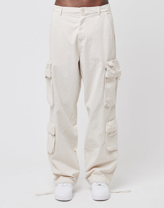 A person wearing the Wide Summer Cargo pants by LIVE FAST DIE YOUNG—a loose, light beige 100% cotton style with multiple cargo pockets—and white sneakers stands against a plain white background.