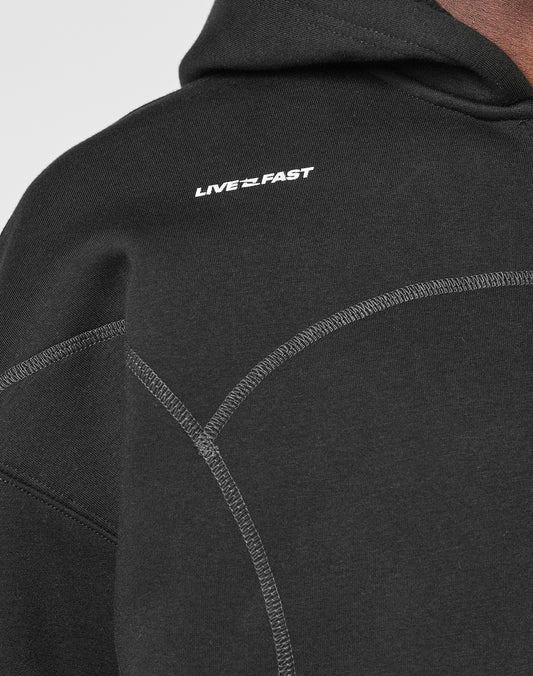 Close-up of the LFDY Active Fleece Hooded Zip by LIVE FAST DIE YOUNG—a black oversized hoodie made from soft Baumwolle, featuring gray stitching and a white LIVE FAST logo print on the chest.