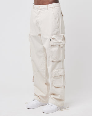 A person wears the LIVE FAST DIE YOUNG Wide Summer Cargo—loose, off-white 100% Baumwolle Ripstop pants with multiple Cargotaschen—paired with white sneakers, standing against a plain white background.