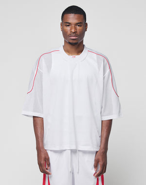 A man faces forward in a LIVE FAST DIE YOUNG Basic Mesh Jersey and matching 100% polyester white mesh shorts with red accents, both in an oversize fit, against a plain light gray background.