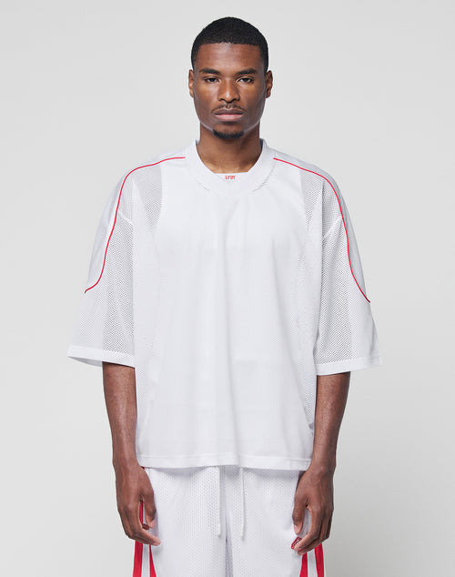 A man faces forward in a LIVE FAST DIE YOUNG Basic Mesh Jersey and matching 100% polyester white mesh shorts with red accents, both in an oversize fit, against a plain light gray background.