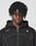 A person with medium-dark skin and tightly coiled hair looks at the camera, wearing the LIVE FAST DIE YOUNG LFDY Active Fleece Hooded Zip—an oversize black hoodie with a white logo on the chest—against a plain light background.