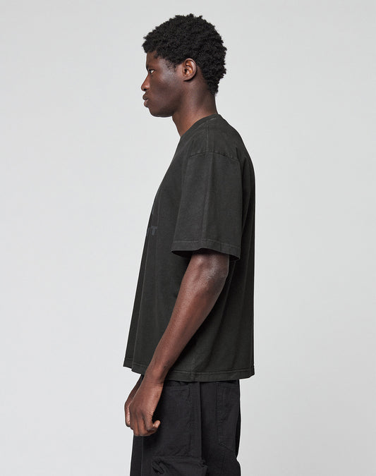 A person with short curly hair stands sideways, facing left, wearing the LIVE FAST DIE YOUNG Live Fast LF Tee in Oversize Fit and black pants against a plain light gray background.