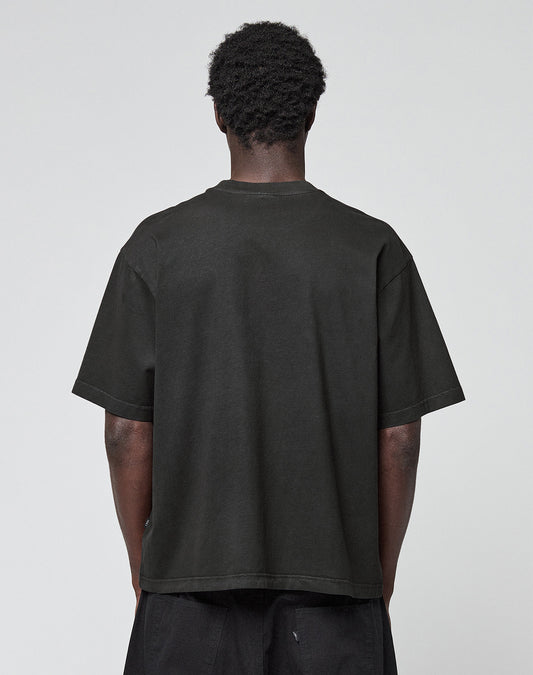 A person with short curly hair stands with their back to the camera, wearing the LIVE FAST DIE YOUNG Live Fast LF Tee in black and matching black pants against a plain light gray background.