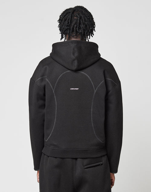 A person with short, twisted hair is shown from the back wearing a black LFDY Active Fleece Hooded Zip and black pants by LIVE FAST DIE YOUNG, featuring light curved seam details and a small white LOST RELIGION logo on the back.