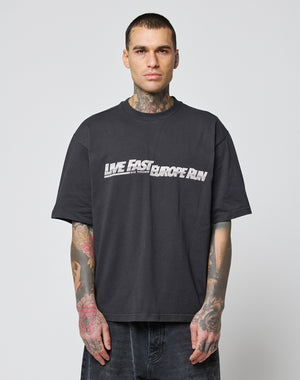 A tattooed man with short hair and a neutral expression wears the LFDY Europe Run Tee by LIVE FAST DIE YOUNG—an oversize black cotton t-shirt featuring LIVE FAST EUROPE RUN in white and gray. Waschhinweise included.