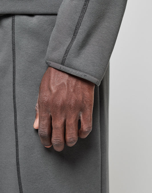 A close-up of a hand and forearm wearing the LIVE FAST DIE YOUNG LFDY Active Fleece Hooded Zip, an oversize-fit gray hoodie with visible seams and subtle logo print, made from 100% Baumwolle, set against a neutral background.