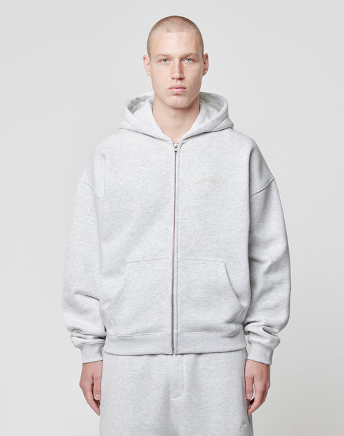 A person with a shaved head wears the LIVE FAST DIE YOUNG Basic Script Hooded Zip and matching sweatpants in light gray, both with a subtle Logo-Stick, standing against a white background and facing the camera neutrally.