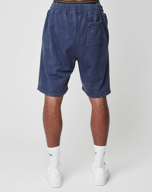 A person stands facing away in LIVE FAST DIE YOUNG LFDY Bulge Shorts in navy with vintage wash, elastic waistband, single back pocket, paired with white socks and sneakers, set against a plain white background.