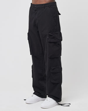 A person wears the LIVE FAST DIE YOUNG Wide Summer Cargo in black with multiple cargo pockets and white sneakers, standing against a plain white background.