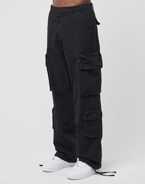 A person wears the LIVE FAST DIE YOUNG Wide Summer Cargo in black with multiple cargo pockets and white sneakers, standing against a plain white background.