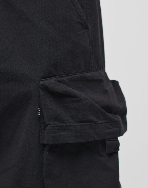 Close-up of a Wide Summer Cargo pant pocket by LIVE FAST DIE YOUNG, made from black ripstop fabric with a flap and small black tag on the side seam, shown against a plain light background.