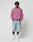 A person stands against a plain background wearing a pink LIVE FAST DIE YOUNG Live Fast Rivet Hooded Zip with handgefertigtem Sprayeffekt, light blue baggy denim shorts, white crew socks, and white sneakers.