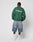A person faces away, wearing the green LFDY Europe Run Sweater by LIVE FAST DIE YOUNG with back print, light blue knee-length denim shorts, white crew socks, and white sneakers, set against a plain white background.