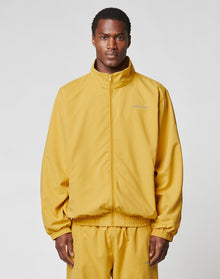 A man wears the LIVE FAST DIE YOUNG LFDY Trackjacket in an oversize fit, mustard yellow with reflective print, along with matching pants. He stands facing forward against a plain light gray background. | model
