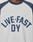 Close-up of a person wearing the Live Fast Raglan Tee by LIVE FAST DIE YOUNG, a boxy oversize fit white shirt with dark raglan sleeves and bold navy "LIVE FAST DY" text, with "DY" centered below "LIVE FAST.