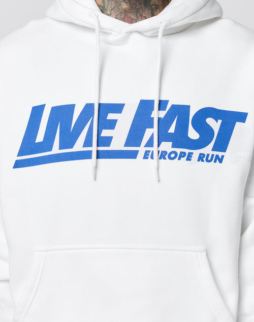 Wearing the Live Fast Europe Run Hooded by LIVE FAST DIE YOUNG in oversize fit and white, with blue LIVE FAST EUROPE RUN text across the chest. Only the lower face and upper torso are shown.