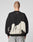 A person with a shaved head faces away wearing the LIVE FAST DIE YOUNG LFDY Mystic Sweater, an oversized black cotton sweatshirt with a white abstract back pattern, topstitching, small white neckline text, and paired with light gray jeans.