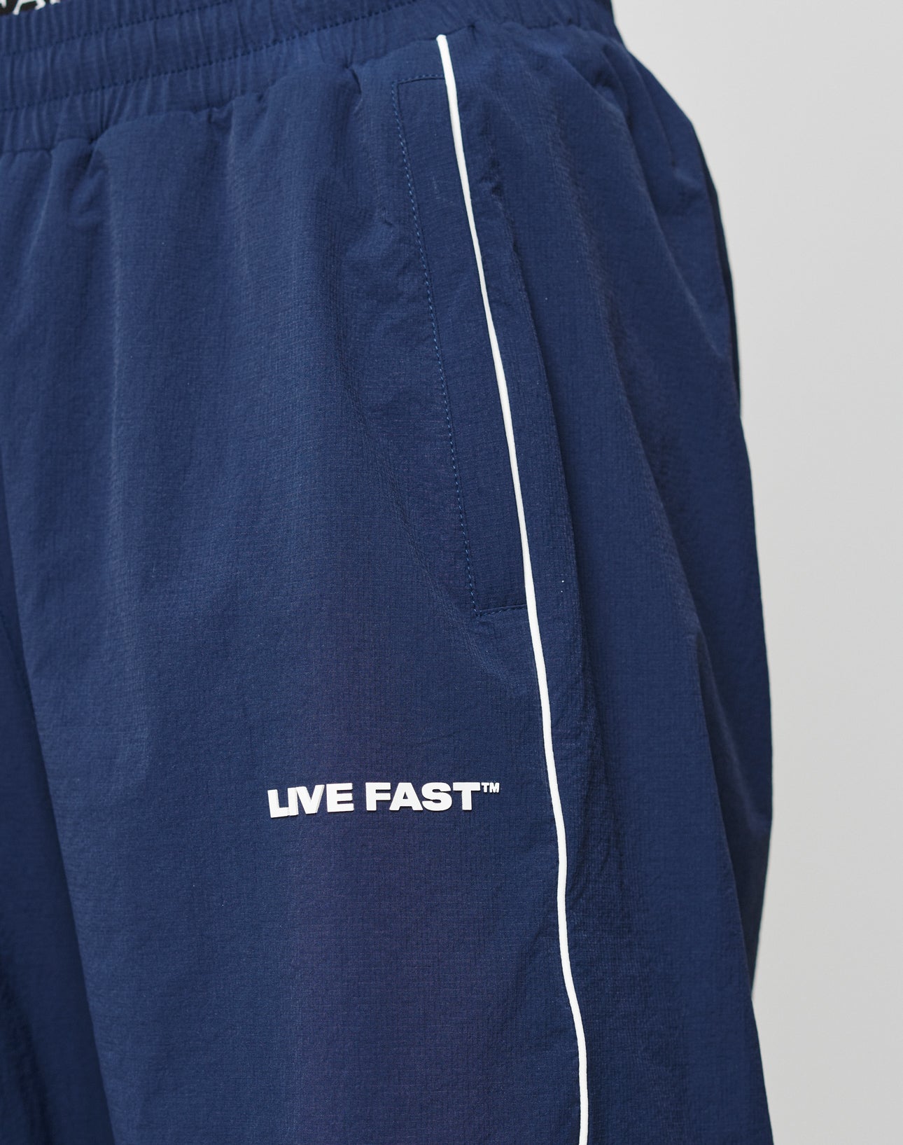 Close-up of LFDY Ripstop Trackpants by LIVE FAST DIE YOUNG in navy, featuring a comfortable Elastik-Bund, white side piping, and LIVE FAST™ in white silikonprint above the left pocket.