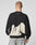 A person with short hair, seen from behind, wears the LFDY Mystic Sweater by LIVE FAST DIE YOUNG—black with white abstract patterns and LIVE FAST text on the upper back—paired with light gray Oversize Fit jeans against a plain background.