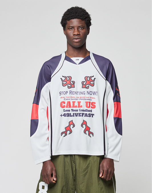 A young man stands facing forward wearing the LIVE FAST DIE YOUNG LFDY Call Us Jersey, an oversize white long-sleeve shirt with blue and red accents, flame graphics, and bold text. He pairs it with olive green shorts.