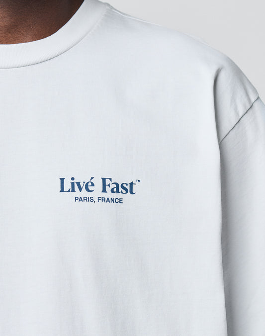 A close-up of the LIVE FAST DIE YOUNG LFDY Paris Tee in white Baumwolle shows Livé Fast™ PARIS, FRANCE in blue on the left chest. Only part of the neck and shoulder are visible, emphasizing its Oversize Fit.