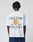 A person wearing the LFDY Paris Tee by LIVE FAST DIE YOUNG, an oversized white cotton T-shirt with blue and yellow front and back graphics reading “Live Fast™ Paris, France” and French text, stands against a plain light background.