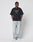 A person stands against a white background, wearing the LIVE FAST DIE YOUNG LFDY Triple Racing Tee—an oversize black graphic T-shirt made of 100% cotton—paired with light blue baggy jeans and white sneakers, hands in pockets, looking aside.