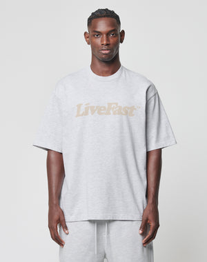 A man faces forward in a light gray LIVE FAST DIE YOUNG Basic Tee featuring LiveFast in beige on the chest, paired with matching light gray shorts, all set against a plain white background.