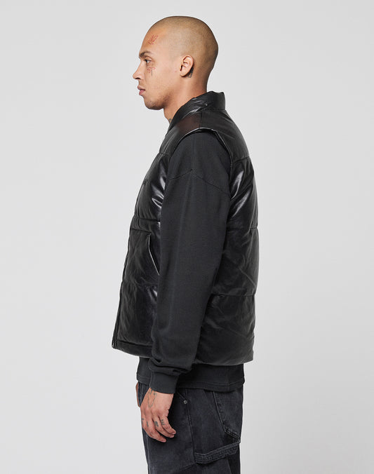 A man with a shaved head stands in profile against a plain background, wearing a black long-sleeve shirt, dark pants, and a regular fit Padded Vest with padded stand-up collar by LIVE FAST DIE YOUNG.