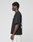 A young man with short curly hair stands in profile against a plain background, wearing the LIVE FAST DIE YOUNG LFDY Real Ones Tee—an oversize black T-shirt aus 100% Baumwolle with bold white front and back prints—and light-colored shorts.
