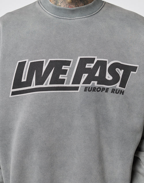 The LIVE FAST DIE YOUNG Live Fast Europe Run Sweater is a grey oversized sweatshirt with vintage wash, bold black LIVE FAST front print, and a smaller EUROPE RUN text across the chest.