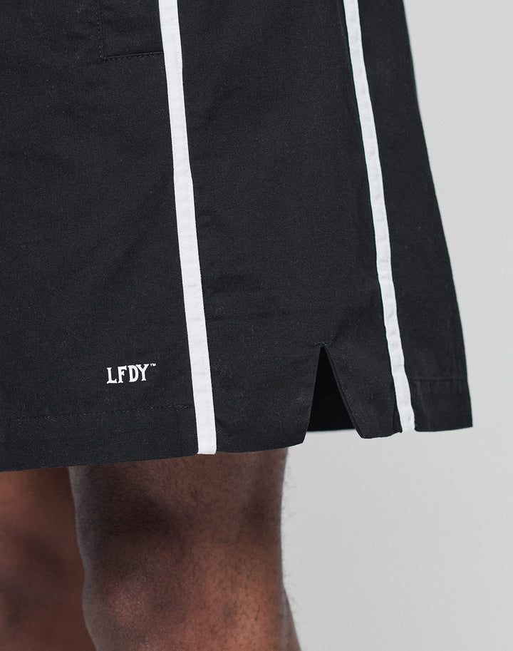 Close-up of a person wearing Basic Cotton Shorts by LIVE FAST DIE YOUNG, featuring a regular fit, black color with white vertical stripes, elastic waistband, front slit, and white LFDY logo print near the above-the-knee hem.