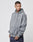 A man with short hair and tattoos wears the LIVЕ FAST DIE YOUNG Basic Heavy Hooded sweatshirt in Oversize Fit, gray with a small white logo, made from soft Baumwolle, paired with dark pants against a plain light background.