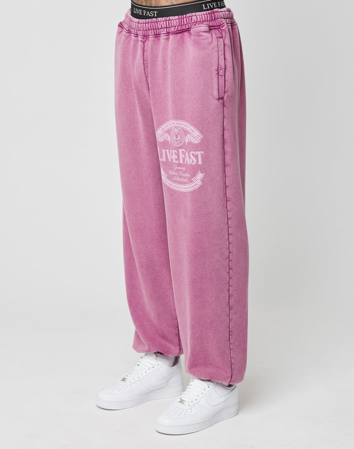 A person wears the Loyal Loose Jogger by LIVE FAST DIE YOUNG—oversized pink sweatpants with a white LIVE FAST print on one leg, made of soft Baumwolle—paired with white sneakers. Only their lower half is visible against a plain background. | model