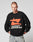 A person with short hair wears the black LFDY Hardwear Sweater by LIVE FAST DIE YOUNG, featuring an orange Pufferprint graphic and white LIVE FAST HARDWEAR text, standing with hands in light blue jean pockets against a plain background.