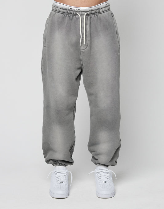 A person models the LIVE FAST DIE YOUNG Basic Loose Joggerālight gray with a subtle logo and elastic waistbandāpaired with white sneakers, standing against a plain light gray background.