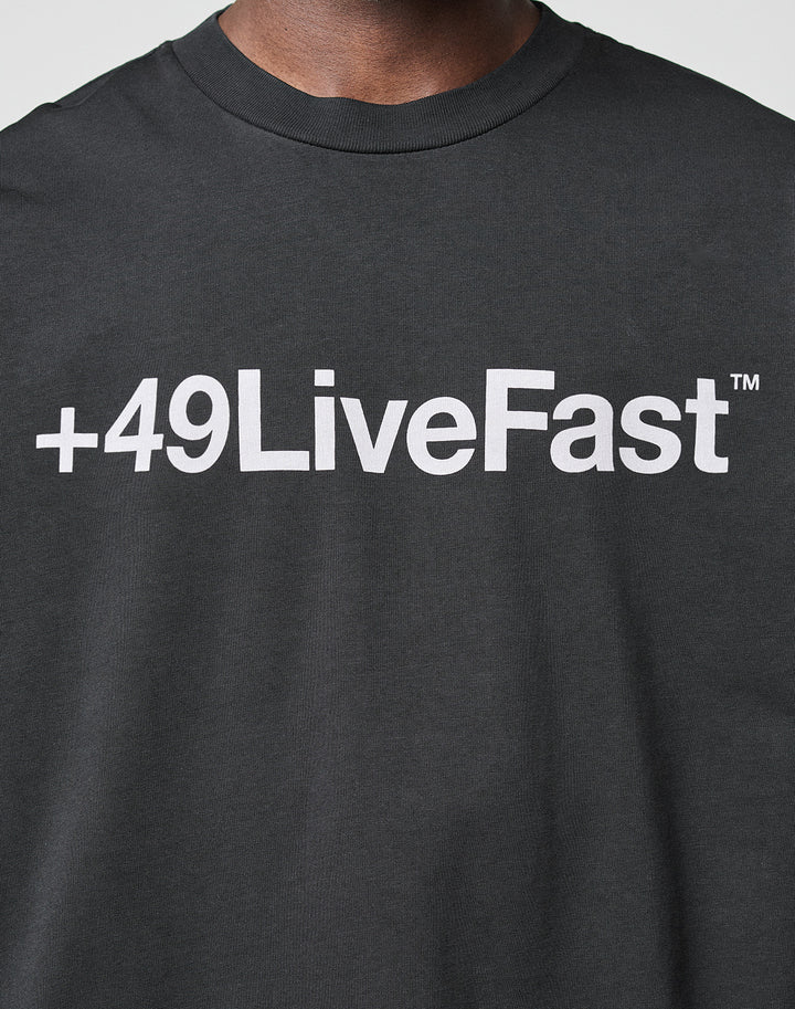 A person wearing the Basic +49 Tee by LIVE FAST DIE YOUNG, featuring an oversize fit, dark color, and bold white +49LiveFast™ front print, made from 100% Baumwolle.