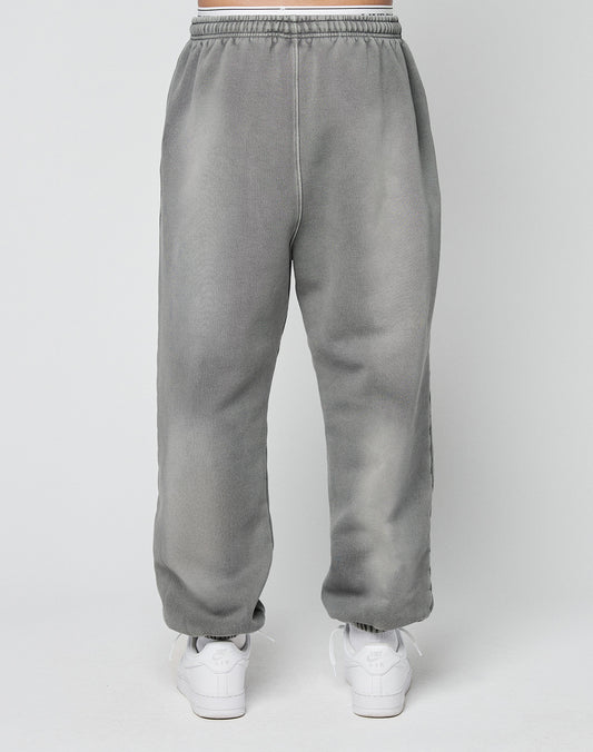 A person models the LIVE FAST DIE YOUNG Basic Loose Joggerāgray sweatpants with an elastic waistbandāpaired with white athletic shoes, standing against a plain light background.