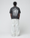 A person faces away, wearing the LIVE FAST DIE YOUNG LFDY Grand Theft Tee—an oversized black T-shirt with bold white graphics on front and back—paired with loose white pants against a plain light background.