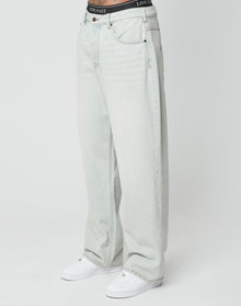 A person in LIVE FAST DIE YOUNGs LFDY Baggy Denim light-wash jeans, white sneakers, and a visible black LIVE FAST waistband stands against a plain white background.