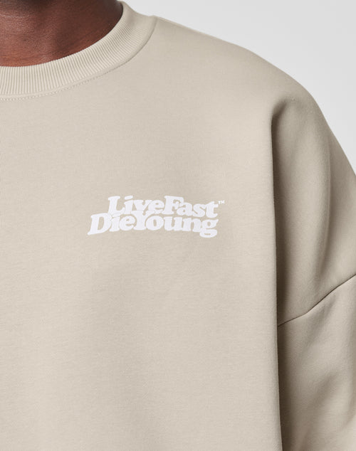 Close-up of the Basic Chest Sweater by LIVE FAST DIE YOUNG in beige Oversize Fit, crafted from soft cotton-polyester blend, featuring bold white Live Fast Die Young front print on the left chest with visible shoulder and neck.