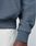Close-up of a person wearing the blue LFDY Guaranteed Hooded Zip by LIVE FAST DIE YOUNG, paired with off-white pants. Part of their hand and arm is visible against a neutral background.