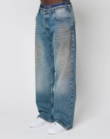 Someone wearing LIVE FAST DIE YOUNG LFDY Tire Tracks Denim, baggy fit, light blue, slightly faded 100% Baumwolle jeans with a high waist, white sneakers, and black LIVE FAST waistband underwear against a plain white background.